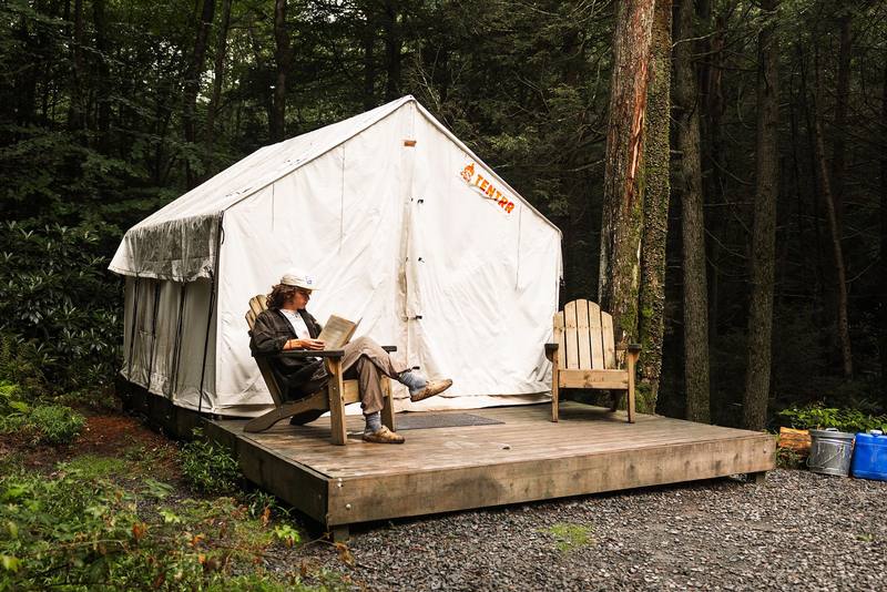 A guest relaxing in an Adirondack chair on a tent deck
