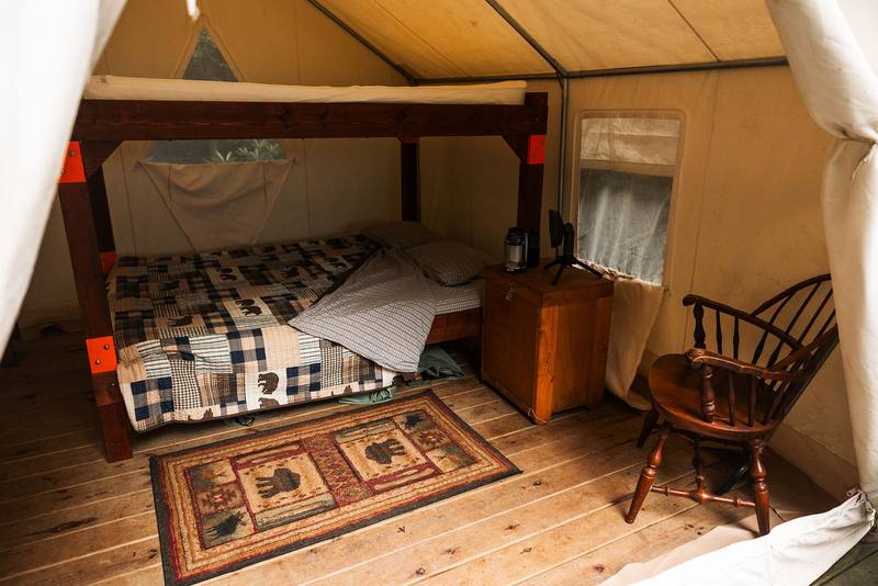 Inside a safari tent: queen bunk bed with plaid quilts, a rug, and a wooden chair